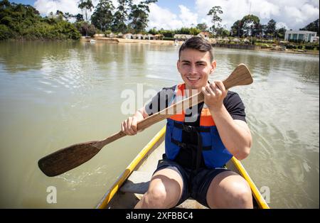 Lächelnder Mann in Schwimmweste, der auf einem kleinen See paddelt Stockfoto