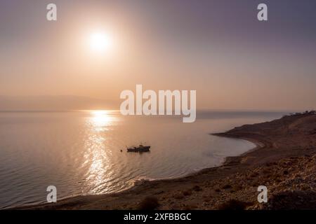 Das einzige Fischerboot auf dem Wasser des Toten Meeres in der Nähe der israelischen Küste (ein Gedi) während des farbenfrohen Sonnenuntergangs im Nahen Osten. Stockfoto