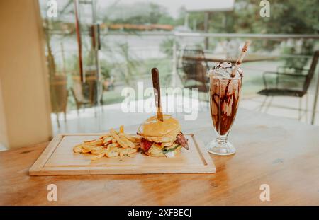 Klassischer Burger mit Pommes frites und Milchshake auf Holzbrett mit Kopierraum. Großer Hamburger mit Pommes und Milchshake auf Restauranttisch Stockfoto