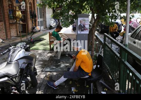 Teheran, Iran. Juli 2024. Ein iranischer Arbeiter sitzt neben einem Wahlplakat für den iranischen Präsidentschaftskandidaten Masoud Pezeshkian in der Innenstadt von Teheran vor der zweiten Wahlrunde bei den Präsidentschaftswahlen. Die zweite Runde der Präsidentschaftswahlen im Iran findet am 5. Juli 2024 statt. Der Reformkandidat Masoud Pezeshkian wird in einer Stichprobe mit dem ultrakonservativen Saeed Jalili konfrontiert sein. (Kreditbild: © Rouzbeh Fouladi/ZUMA Press Wire) NUR REDAKTIONELLE VERWENDUNG! Nicht für kommerzielle ZWECKE! Stockfoto