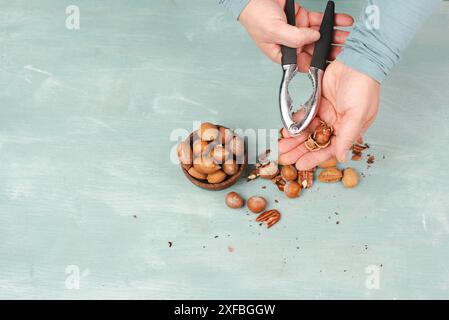 Nüsse mit einem Nussknacker knacken, verschiedene Mandeln, Haselnüsse und Pekannüsse mischen, gesunde Ernährung und Lebensstil Stockfoto