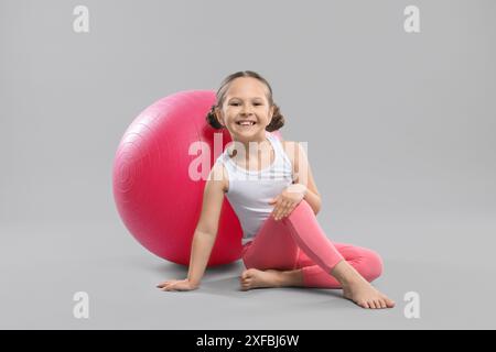 Niedliches kleines Mädchen mit passendem Ball auf grauem Hintergrund Stockfoto