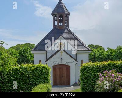 Eine kleine Kirche mit Glockenturm und Uhr inmitten eines gepflegten Gartens unter blauem Himmel, Stein, schleswig. deutschland Stockfoto