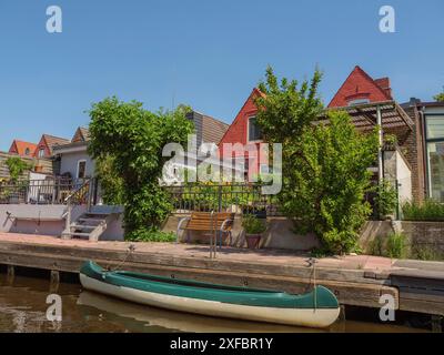 Häuser am Kanal mit einem geparkten Boot im Vordergrund und üppiger grüner Vegetation, friedrichstadt, schleswig-holstein, deutschland Stockfoto