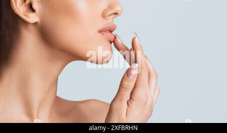 Frau, Die Lippe Sanft Mit Dem Finger Auf Blauem Hintergrund Berührt Stockfoto