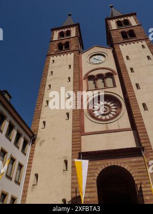 Eine beeindruckende Kirche mit zwei hohen Türmen und gotischen Steinfassaden, die sich vor einem klaren blauen Himmel abheben, würzburg, bayern, deutschland Stockfoto