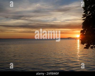 Ein malerischer Sonnenuntergang über einem See, mit orangefarbenem Himmel und Bäumen, lindau, bayern, deutschland Stockfoto