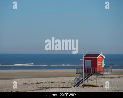 Ein roter Rettungsturm steht an einem ruhigen Strand vor einem blauen Meer unter einem klaren blauen Himmel, langeoog6 Stockfoto