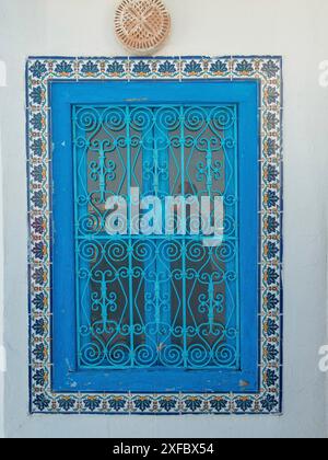 Blaues, vergittertes Fenster, eingerahmt von gemusterten Fliesen an einer Wand, Tunis, Tunesien Stockfoto