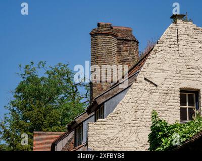 Ein altes Backsteinhaus mit Kamin, Fenstern und umliegenden Bäumen unter blauem Himmel, Brügge, Flandern, Belgien Stockfoto