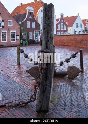 Ein rustikaler Anker und eine Kette auf einem Kopfsteinpflaster vor traditionellen Backsteinhäusern, Greetsiel, Ostfriesland, Deutschland Stockfoto