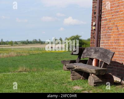 Neben einer Backsteinmauer steht eine rustikale Holzbank auf einer grünen Wiese in ländlicher Umgebung, Greetsiel, Ostfriesland Stockfoto