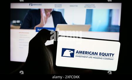 Person, die ein Mobiltelefon hält, mit dem Logo der American Equity Investment Life Holding Company vor der Webseite des Unternehmens. Schwerpunkt auf dem Display des Telefons. Stockfoto