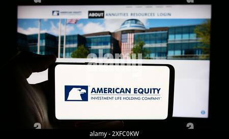 Person, die ein Mobiltelefon hält, mit dem Logo der American Equity Investment Life Holding Company vor der Webseite des Unternehmens. Schwerpunkt auf dem Display des Telefons. Stockfoto