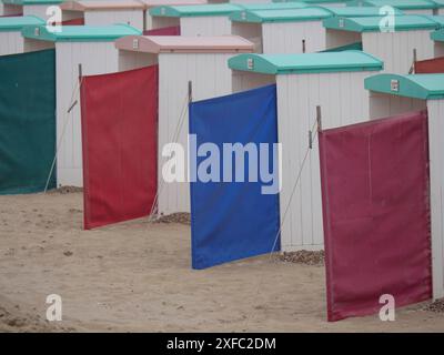 Farbenfrohe vertikale Planen vor weißen Strandhütten an einem Sandstrand, Leiden, Niederlande Stockfoto