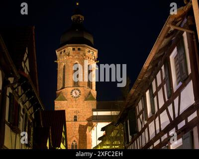 Beleuchteter Kirchturm zwischen Fachwerkhäusern in einer Dorfszene bei Nacht, kandel, deutschland Stockfoto