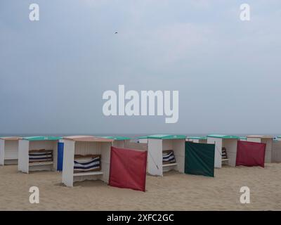 Mehrere Strandhütten mit bunten Bezügen säumen einen Sandstrand unter grauem Himmel, Juist, ostfriesland, deutschland Stockfoto