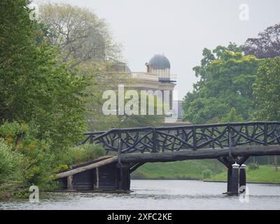 Eine hölzerne Brücke in einem nebeligen Park, die zu einem Gebäude mit einem Turm führt und von dichten Bäumen umgeben ist, Leiden, Niederlande Stockfoto