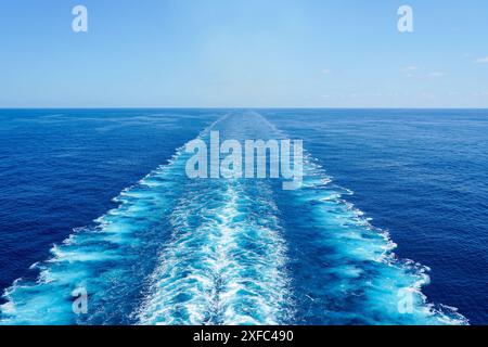 Breiter turbulenter weißer Schaumwasserpfad hinter einem großen Kreuzfahrtschiff in einem ruhigen blauen Meer, Ozean an einem sonnigen Tag, blauer Himmel über dem Horizont Stockfoto