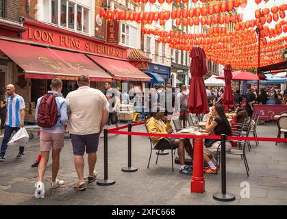 London / UK - 28. Juni 2024: Menschen sitzen in Straßenrestaurants und laufen unter roten Laternen in Chinatown in London. Stockfoto