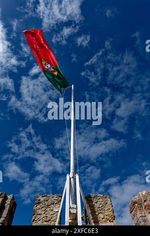Die portugiesische Flagge fliegt hoch über den Steinmauern des Castelo de São Jorge, der vor einem leuchtend blauen Himmel steht Stockfoto