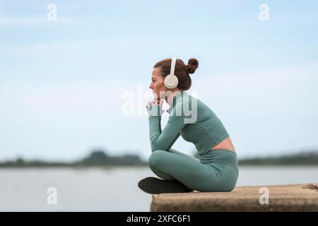 Sportliche Frau, die sich nach dem Training ausruht und Kopfhörer trägt, sieht nachdenklich aus Stockfoto