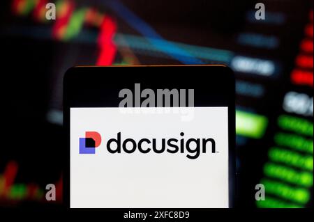 In dieser Fotoabbildung wird das Logo des amerikanischen Softwareunternehmens DocuSign (NASDAQ: DOCU) auf einem Smartphone mit einem Index der wirtschaftlichen Börsen im Hintergrund dargestellt. Stockfoto