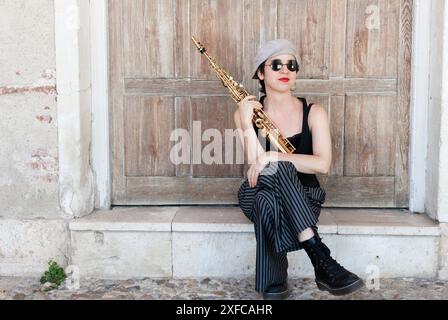 Jazzmusiker im Retro-Stil spielen auf der Straße. Eine brünette Frau mit Mütze und Sonnenbrille, die Saxophon im Vordergrund und im B spielt Stockfoto