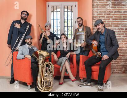 Jazzband bestehend aus 6 Mitgliedern, die auf einem orangen Sessel in einer Bar sitzen und ihre jeweiligen Musikinstrumente tragen. Stockfoto