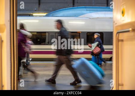 Unscharfe Bewegungen von Passagieren mit Gepäck, die auf dem Bahnsteig am Bahnhof Santa Justa in Sevilla, Spanien, laufen. AVE-Zug im Hintergrund. Stockfoto