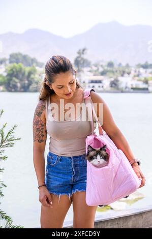 Trendige tätowierte Frau, die einen Tag mit ihrer geliebten Katze in einem rosa Sling Bag genießt Stockfoto