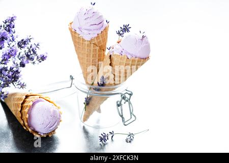 Zwei cremige Lavendeleis in einem Waffelkegel in einem Glasgefäß mit Lavendelblüten. Leerzeichen für Text. Gesundes Dessert gefroren Stockfoto