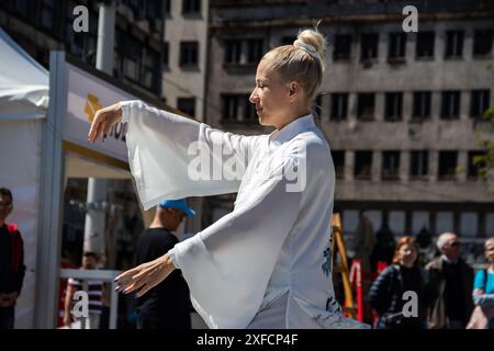 Eine ruhige Tai-Chi-Meisterin in einem fließenden weißen Anzug tritt anmutig auf einer belebten Straße auf, ihre fließenden Bewegungen stehen im Kontrast zur lebendigen städtischen Kulisse Stockfoto