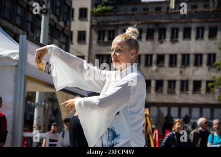 Eine ruhige Tai-Chi-Meisterin in einem fließenden weißen Anzug tritt anmutig auf einer belebten Straße auf, ihre fließenden Bewegungen stehen im Kontrast zur lebendigen städtischen Kulisse Stockfoto