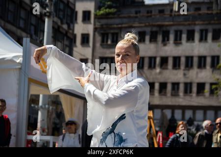 Eine ruhige Tai-Chi-Meisterin in einem fließenden weißen Anzug tritt anmutig auf einer belebten Straße auf, ihre fließenden Bewegungen stehen im Kontrast zur lebendigen städtischen Kulisse Stockfoto