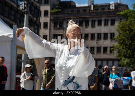 Eine ruhige Tai-Chi-Meisterin in einem fließenden weißen Anzug tritt anmutig auf einer belebten Straße auf, ihre fließenden Bewegungen stehen im Kontrast zur lebendigen städtischen Kulisse Stockfoto