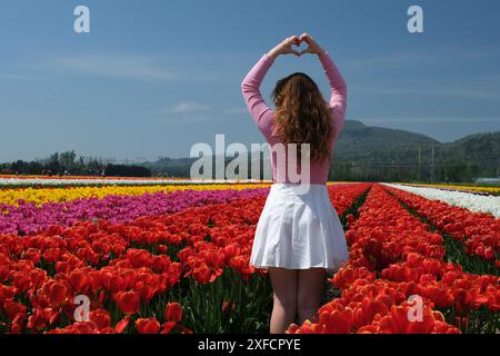 Attraktive Frau in einem hübschen Blumenkleid, die im Frühling durch endloses Tulpenfeld läuft. Luftaufnahme von bunten Tulpen in Blüte und Mädchen. Konzept: Tulpen in den Gärten des Keukenhof, Niederlande, Holland. Stockfoto