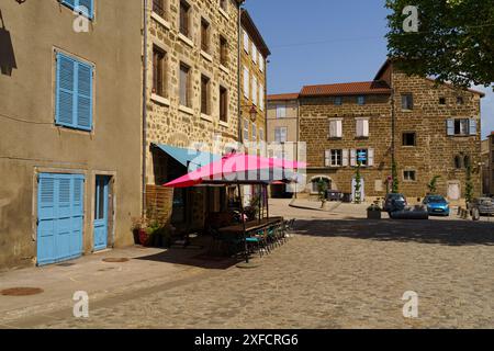 Langeac, Frankreich - 28. Mai 2023: Ein leuchtend rosafarbener Regenschirm spendet Schatten über einem Café im Freien auf dem charmanten Marktplatz von Langeac, Frankreich. Steinbügel Stockfoto