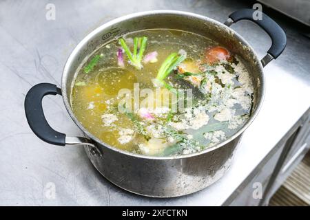 Gekochte Daunenbrühe aus Gemüseresten und Geflügelzubereitungen mit Proteinschaum und Fettaugen in einem großen Edelstahltopf auf einem professionellen k Stockfoto