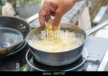 Geben Sie ein Stück panko paniertes Hühnchen von Hand in einen Topf mit heißem kochendem Öl zum Frittieren, Kochen in einer Außenküche, ausgewählter Fokus, schmales d Stockfoto