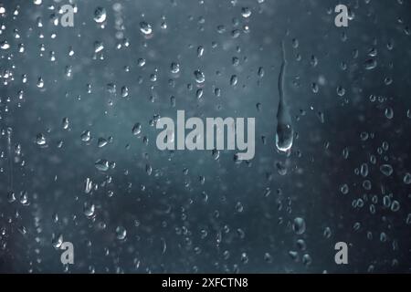 Regentropfen, die an einem dunklen, regnerischen Tag durch eine Fensterscheibe laufen, Vollformathintergrund, Konzept für deprimierendes Wetter, Kopierraum, ausgewählter Fokus Stockfoto