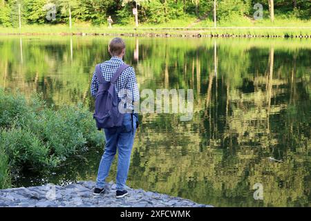 Fischer stehend mit einer Angelrute, Rückansicht. Mann, der an der Seeküste im Sommerpark angeln kann Stockfoto