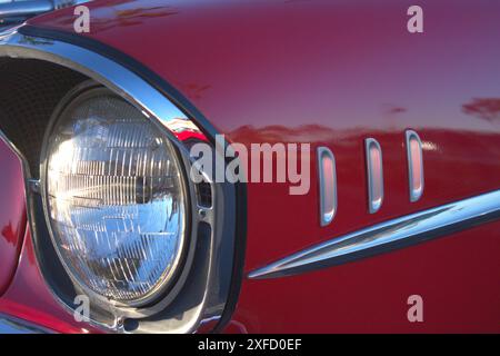 Ein detailliertes Foto des Frontscheinwerfers auf der Fahrerseite und des Kotflügels eines klassischen roten 1957 Chevy Bel Air. Stockfoto