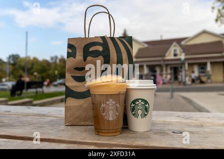 Zwei Starbucks-Drinks vor der Papiertüte - Holztisch im Freien - mit Karamell-Nieseln vereist - verschwommenes Gebäude und Baumhintergrund. Aufgenommen in Toront Stockfoto