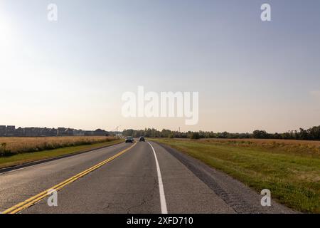 Offene Straße vor Ihnen, helle Sonne - Auto fährt in die Ferne - üppiges Grün an den Seiten. Aufgenommen in Toronto, Kanada. Stockfoto