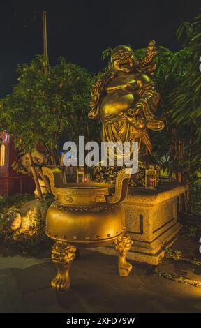 Jakarta, Indonesien - 11. Mai 2024. Ein Nahaufnahme-Foto einer goldenen Statue eines lachenden Buddha in einem ruhigen Garten bei Nacht. Das Lächeln und der Post der Statue Stockfoto