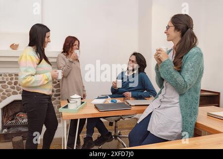Vier Kollegen machen eine Pause im Büro, genießen Kaffee und unterhalten sich. Sie haben Spaß und entspannen sich zusammen und schaffen eine freundliche und positive Atmosphäre Stockfoto