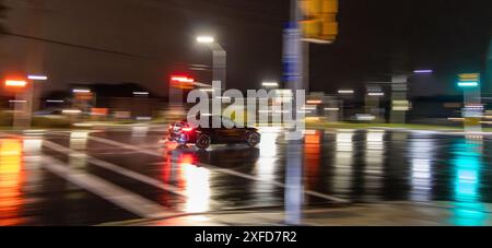 Lebhafte Nachtszene – regendurchflutete Straße reflektiert bunte Lichter – Einzelfahrzeug in Bewegung unscharf. Aufgenommen in Toronto, Kanada. Stockfoto