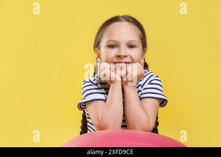 Süßes kleines Mädchen mit passendem Ball auf gelbem Hintergrund Stockfoto