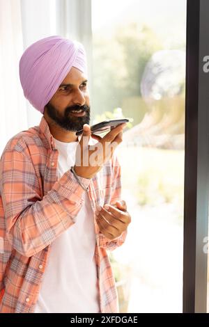 Ich spreche auf dem Smartphone, ein Indianer im Turban, der zu Hause am Fenster steht Stockfoto